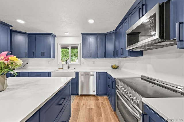 3881 S Bahama St, Aurora, CO 80013 - kitchen with appliances with stainless steel finishes, a sink, blue cabinetry, light wood-type flooring, and recessed lighting