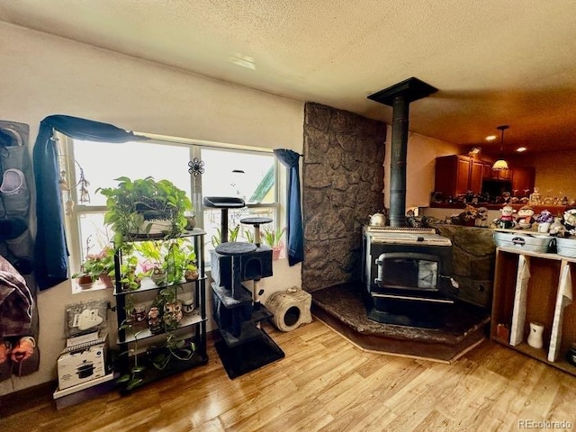 interior space with a textured ceiling, a wood stove, and light wood-type flooring