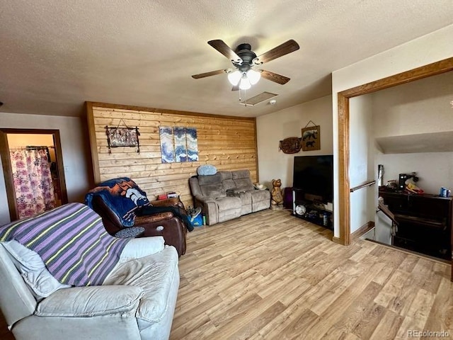 living room with a textured ceiling, wood walls, ceiling fan, and light wood-type flooring