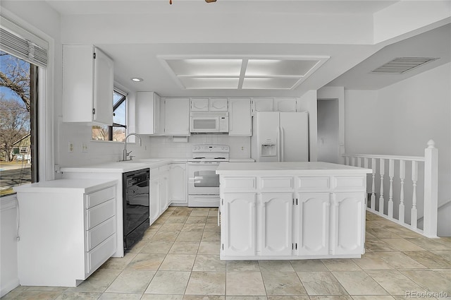 kitchen featuring white appliances, a kitchen island, a sink, visible vents, and white cabinets