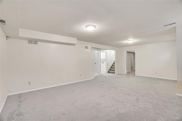 finished below grade area featuring carpet, visible vents, stairway, and a textured ceiling