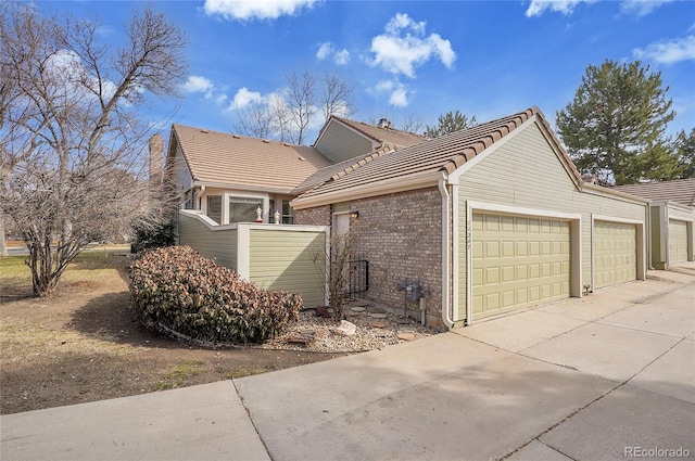 view of side of property with a garage, a tiled roof, brick siding, and concrete driveway