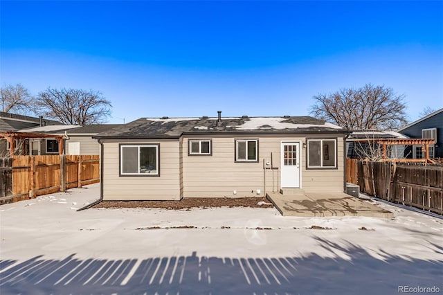 snow covered back of property with a fenced backyard and a patio