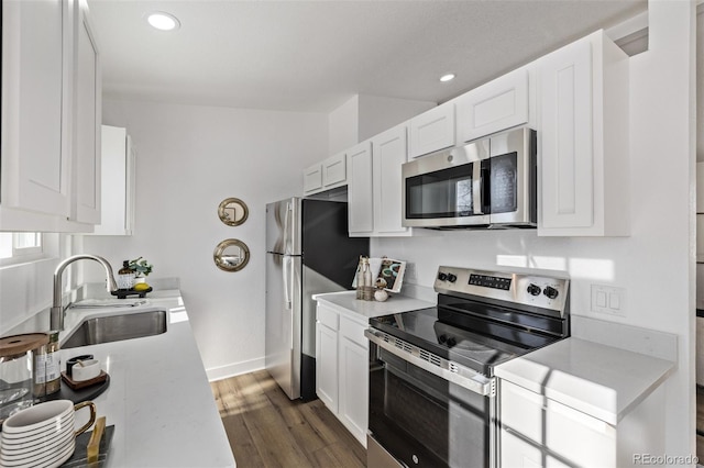 kitchen with a sink, white cabinetry, light countertops, appliances with stainless steel finishes, and dark wood-style floors