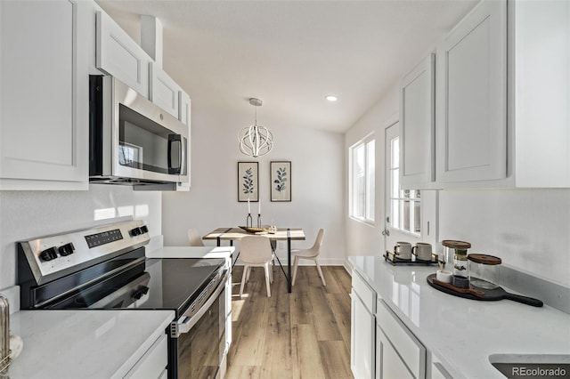 kitchen featuring hanging light fixtures, appliances with stainless steel finishes, wood finished floors, and white cabinets