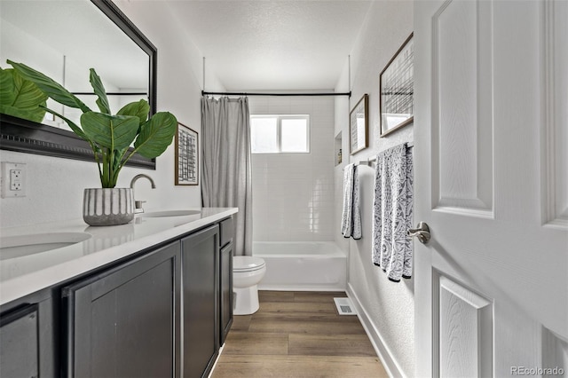 bathroom with double vanity, toilet, wood finished floors, shower / tub combo with curtain, and a sink