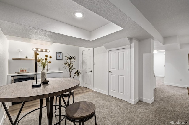 dining space featuring beverage cooler, baseboards, a textured ceiling, and light colored carpet