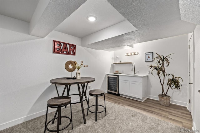 interior space featuring beverage cooler, indoor wet bar, light wood-style flooring, and a textured ceiling