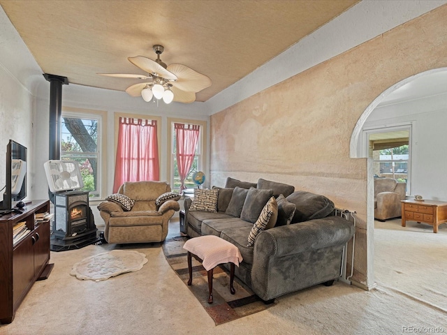 living area featuring a wood stove, a textured wall, a ceiling fan, and light colored carpet