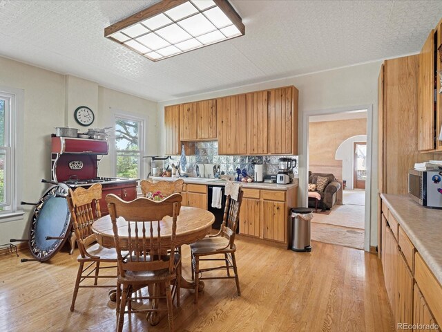 kitchen with light wood-type flooring, black dishwasher, stainless steel microwave, and arched walkways