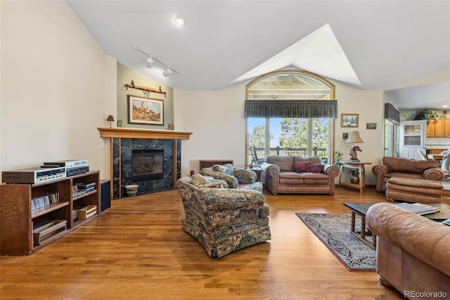 living room with lofted ceiling, light wood-type flooring, a premium fireplace, and track lighting