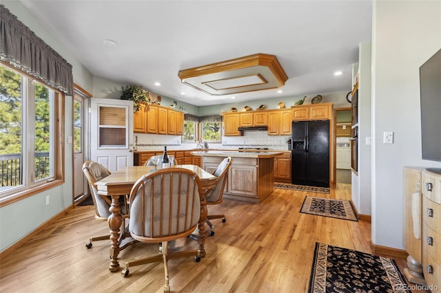 kitchen featuring backsplash, a center island, black refrigerator with ice dispenser, light hardwood / wood-style flooring, and stainless steel oven