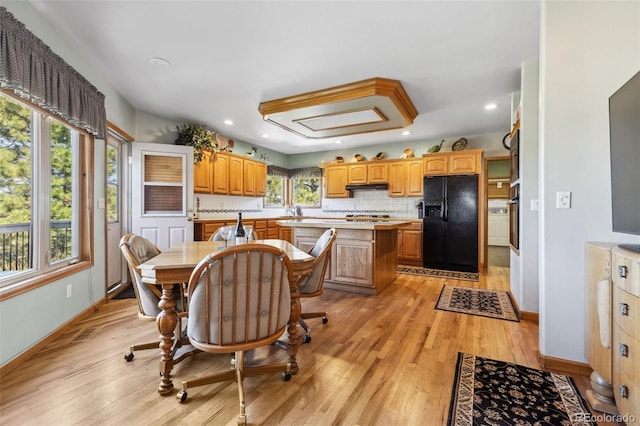 kitchen with oven, light countertops, black refrigerator with ice dispenser, a center island, and light wood finished floors