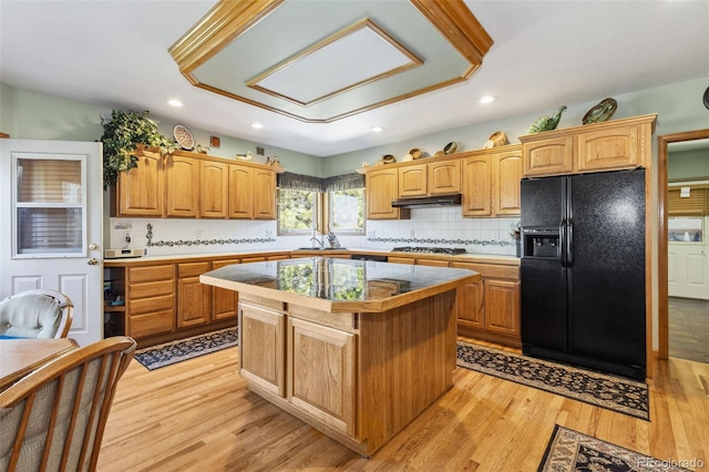 kitchen with tasteful backsplash, light hardwood / wood-style floors, a kitchen island, black refrigerator with ice dispenser, and sink