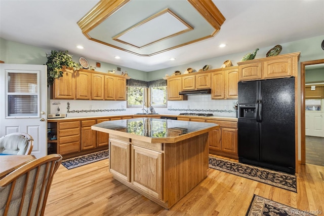 kitchen with a kitchen island, light wood-style floors, black fridge with ice dispenser, and under cabinet range hood