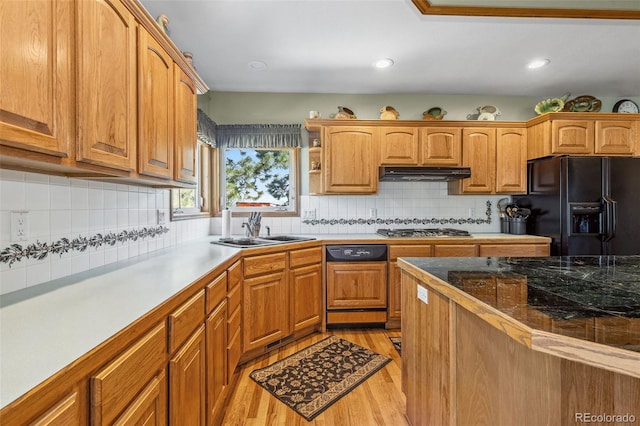 kitchen featuring black fridge with ice dispenser, paneled dishwasher, under cabinet range hood, stainless steel gas cooktop, and a sink
