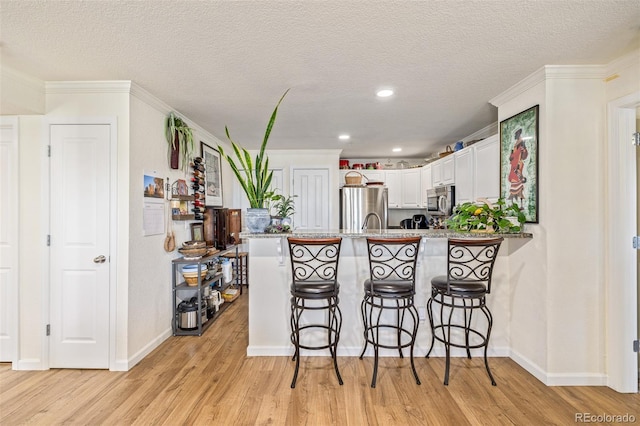 kitchen featuring kitchen peninsula, a kitchen breakfast bar, white cabinetry, light hardwood / wood-style floors, and stainless steel appliances