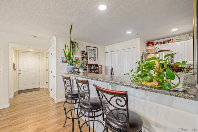 kitchen featuring stone countertops, ornamental molding, light wood-type flooring, white cabinets, and a textured ceiling