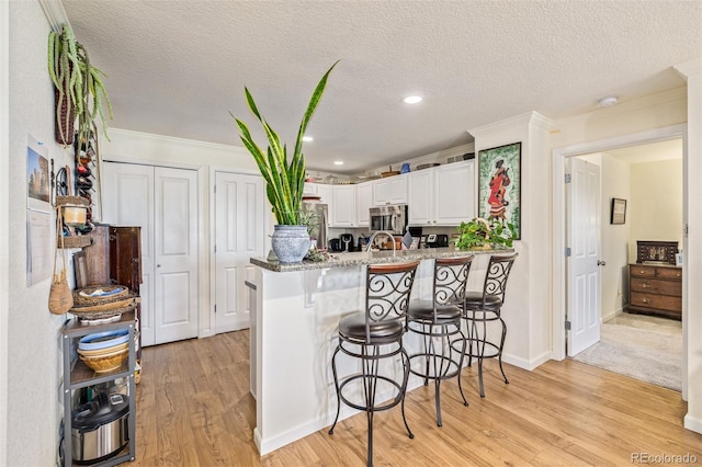 kitchen featuring kitchen peninsula, white cabinetry, a textured ceiling, and light wood-type flooring