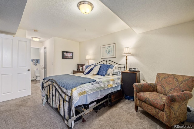 bedroom with ensuite bathroom, a textured ceiling, and light colored carpet