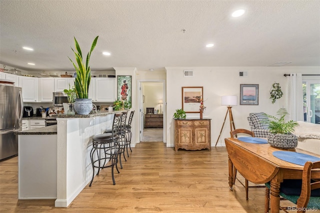 kitchen with a breakfast bar, white cabinets, appliances with stainless steel finishes, a textured ceiling, and light hardwood / wood-style floors