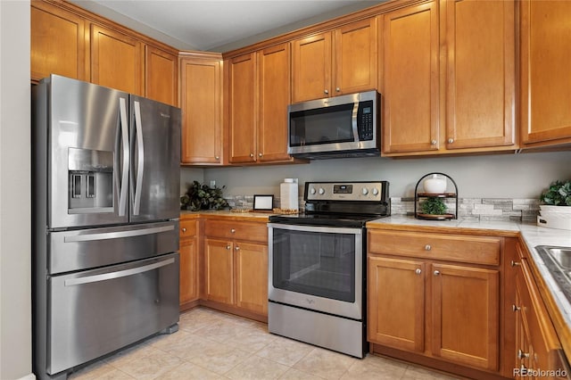 15125 E Bayaud Pl, Aurora, CO 80012 - kitchen featuring stainless steel appliances, brown cabinetry, light tile patterned flooring, and tile counters