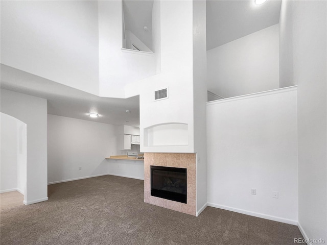 unfurnished living room featuring dark carpet, a fireplace, and a high ceiling