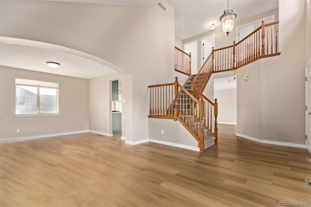 unfurnished living room featuring arched walkways, light wood finished floors, visible vents, and baseboards