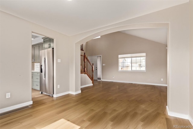 unfurnished living room featuring lofted ceiling, stairway, light wood-style flooring, and arched walkways