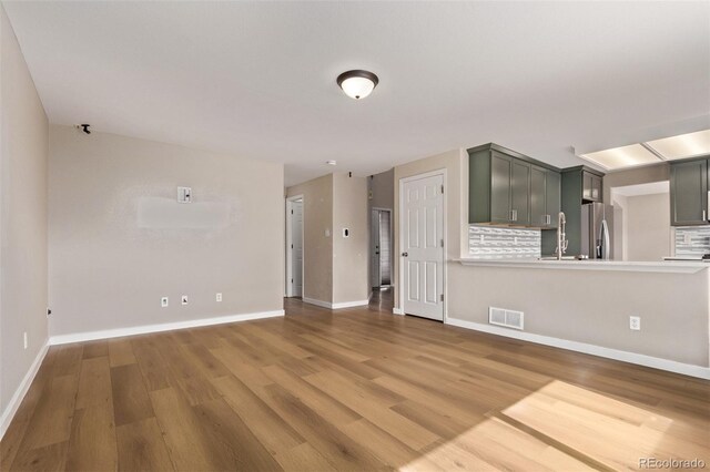 unfurnished living room with light wood finished floors, visible vents, and baseboards