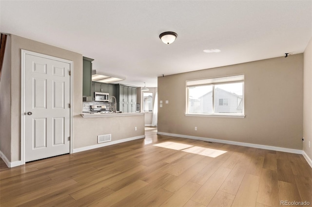 unfurnished living room featuring visible vents, baseboards, and wood finished floors