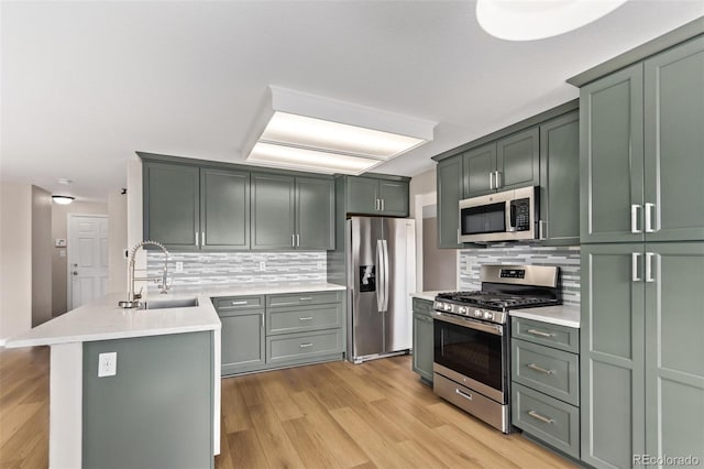 kitchen with stainless steel appliances, light countertops, a sink, light wood-type flooring, and a peninsula