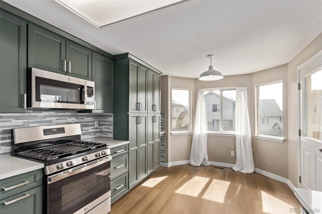 kitchen with stainless steel appliances, light countertops, light wood-type flooring, decorative backsplash, and green cabinetry