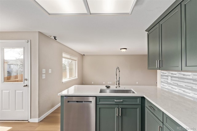 kitchen with a peninsula, a sink, green cabinets, light wood-type flooring, and dishwasher