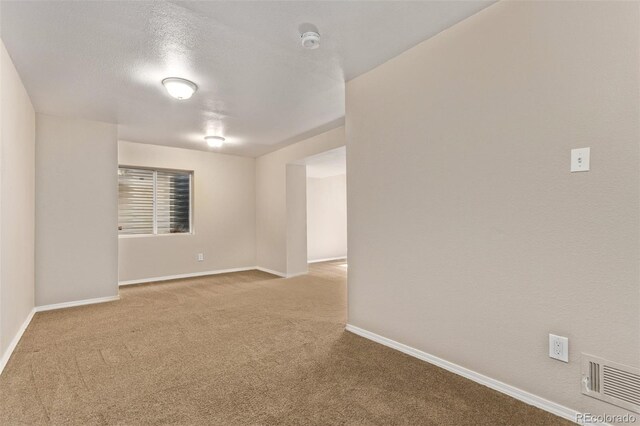 spare room featuring a textured ceiling, carpet, visible vents, and baseboards