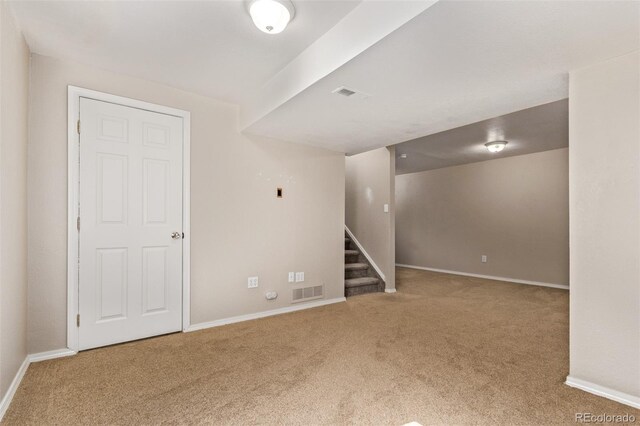 carpeted empty room with visible vents, baseboards, and stairs