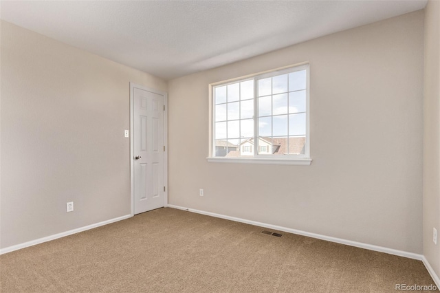 spare room with carpet floors, visible vents, and baseboards