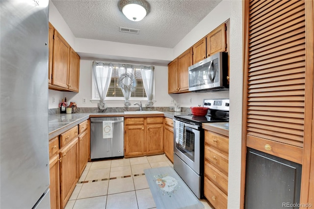 kitchen featuring appliances with stainless steel finishes, a textured ceiling, sink, and light tile patterned floors