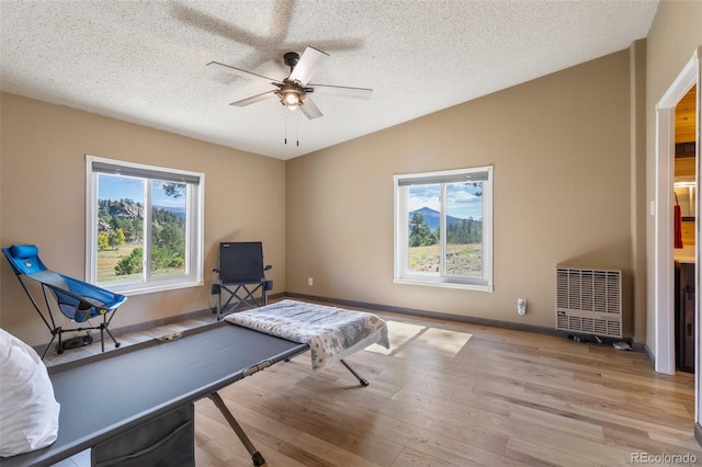 game room with vaulted ceiling, heating unit, a textured ceiling, ceiling fan, and light hardwood / wood-style flooring