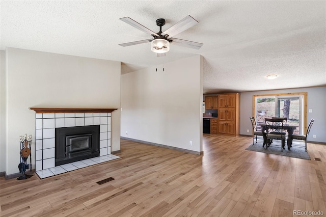 unfurnished living room featuring a tiled fireplace, light hardwood / wood-style floors, ceiling fan, and a textured ceiling