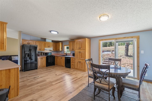 kitchen with a textured ceiling, black appliances, sink, and light hardwood / wood-style flooring