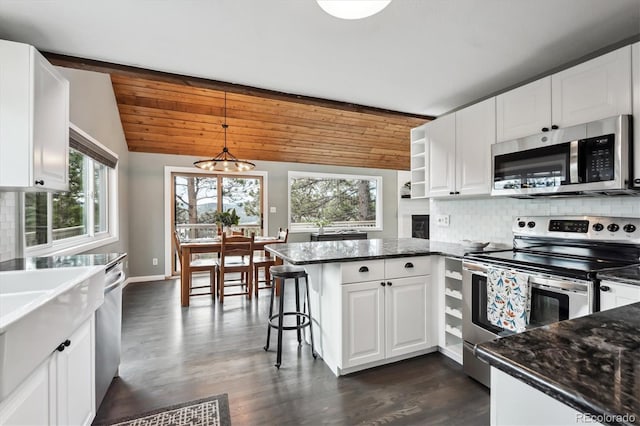 kitchen with appliances with stainless steel finishes, white cabinetry, lofted ceiling, hanging light fixtures, and kitchen peninsula