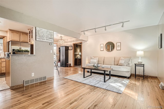 living area with baseboards, visible vents, light wood finished floors, rail lighting, and a notable chandelier