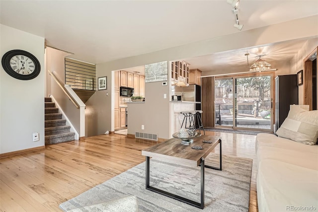 living area with visible vents, stairs, rail lighting, light wood-type flooring, and a chandelier