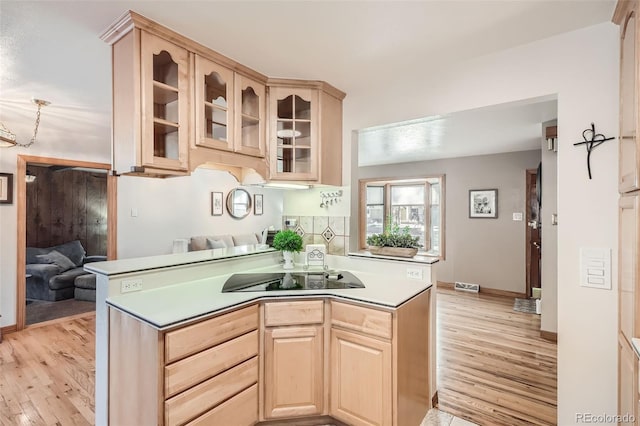 kitchen featuring light wood-type flooring, light brown cabinetry, light countertops, glass insert cabinets, and black electric stovetop