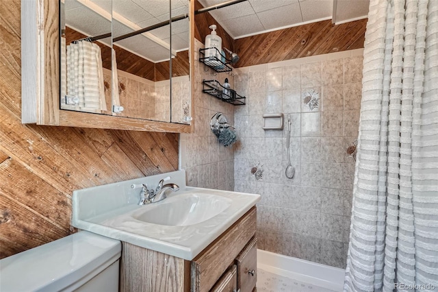 bathroom with wood walls, tiled shower, vanity, and toilet