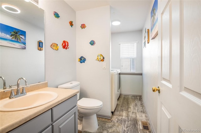 bathroom with hardwood / wood-style flooring, vanity, independent washer and dryer, and toilet