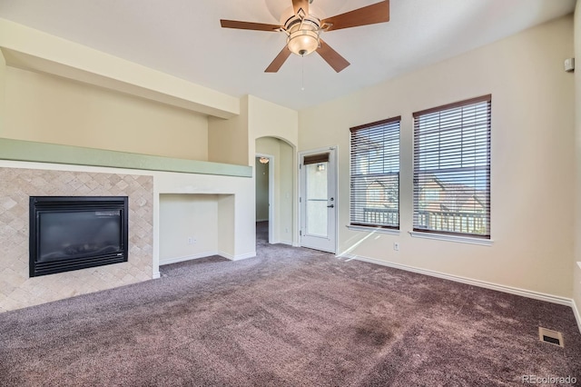 unfurnished living room with a ceiling fan, carpet, baseboards, a fireplace, and arched walkways