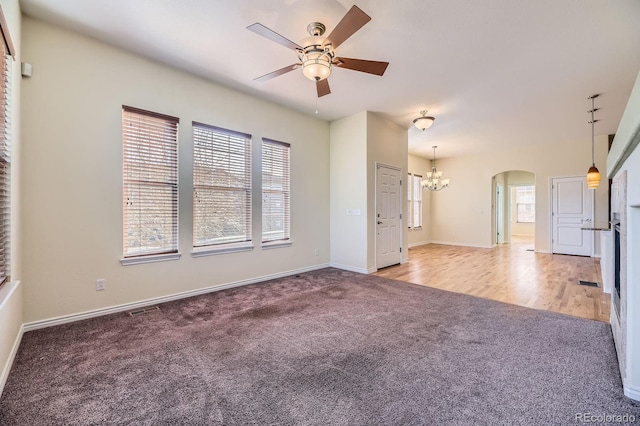 unfurnished living room featuring visible vents, ceiling fan with notable chandelier, arched walkways, carpet floors, and baseboards