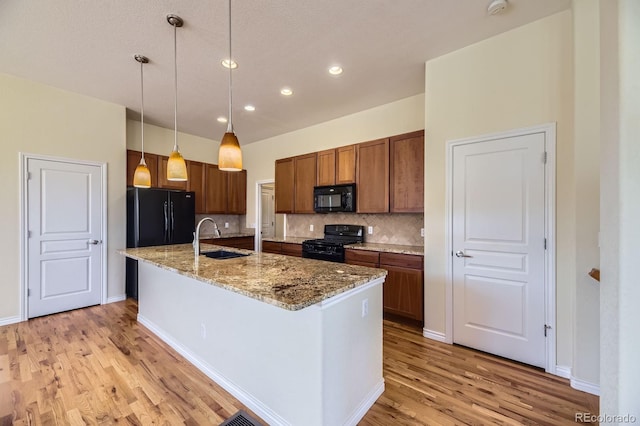 kitchen with a sink, hanging light fixtures, black appliances, light wood-type flooring, and backsplash